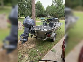 A well-maintained fishing boat with an outboard motor parked on the grass, showcasing its sleek design and readiness for a day on the water.