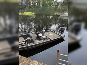 A sleek custom craft boat docked by a serene waterway, showcasing its clean lines and functional design, perfect for fishing or leisurely outings.