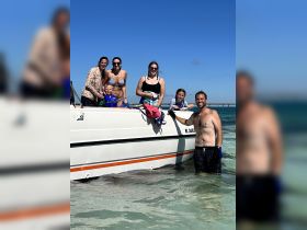 A joyful family poses by their boat in shallow waters, enjoying a fun day out on the water — perfect for creating lasting memories together.