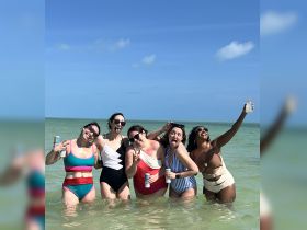 A fun group of friends enjoys a lively day at the beach, celebrating with drinks and laughter in the warm water — perfect for memorable summer outings.
