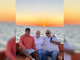 A joyful group enjoys a sunset cruise on a boat, capturing a perfect moment with drinks in hand against a stunning backdrop of the setting sun.