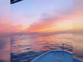 A stunning sunset view from the bow of a boat, showcasing vibrant colors reflecting on calm waters — perfect for evening cruises.