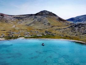 A stunning aerial view of a serene bay with a boat anchored in turquoise waters, surrounded by lush hills — an ideal destination for relaxation and exploration.
