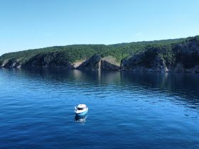 A serene view of a small boat anchored in calm waters, surrounded by lush green cliffs — an ideal setting for peaceful boating adventures.