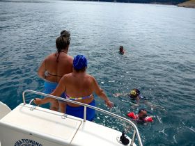 A joyful group enjoys swimming and snorkeling in clear waters, creating unforgettable memories on their boating adventure.