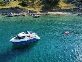 An aerial view of a boat anchored in clear waters, with guests enjoying the sun and a pink floating mat nearby — perfect for a relaxing day on the water.