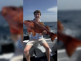 A young angler proudly displays his impressive catch while fishing on the open ocean — a perfect moment for fishing enthusiasts.