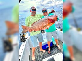 Two anglers proudly display their impressive catch while fishing on a boat, showcasing the thrill of a successful day on the water.