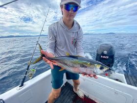 A young angler proudly displays his catch while fishing on the open ocean, showcasing the thrill of sport fishing adventures.