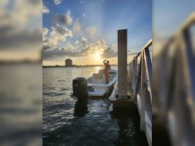 A person stands on a boat at sunset, capturing the serene moment by the dock — a perfect backdrop for evening adventures on the water.
