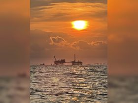 A stunning sunset over the ocean, featuring silhouetted oil rigs against the vibrant sky — a picturesque moment capturing the beauty of nature and industry.