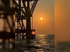 A silhouette of a structure against a sunset over the water, creating a serene yet ambiguous scene.