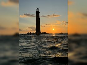A stunning sunset view of a lighthouse silhouetted against the vibrant sky, capturing the serene beauty of the water — perfect for scenic boat trips.