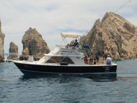A fishing boat with a group of people enjoying their time in Cabo San Lucas, surrounded by stunning rock formations — perfect for an adventurous day on the water.