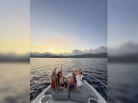 A lively group of friends celebrates on the bow of a yacht at sunset, capturing the essence of fun and friendship on the water.