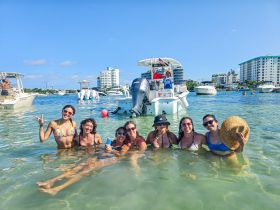 A lively group of friends enjoys a fun day swimming in shallow waters near their boat, capturing the essence of a perfect beach party.