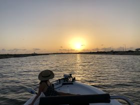 A woman enjoys a serene sunset view from the bow of a boat, capturing the essence of relaxation on the water as day turns to night.