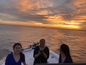 A joyful group of friends enjoys a stunning sunset aboard a boat, capturing memories against a vibrant sky — perfect for unforgettable evening cruises.