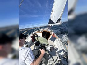 A sailor navigates a yacht while a companion relaxes on deck, showcasing the joy of sailing on open waters.