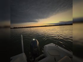 A serene sunset view from a boat, showcasing the engine and calm waters, perfect for evening cruises or fishing trips.