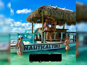A fun group of friends enjoys a sunny day on the Nautical Tiki boat, splashing in the turquoise waters and soaking up the sun — perfect for a lively beach party experience.