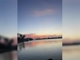 A serene sunset over calm waters, reflecting vibrant colors and palm trees along the coastline — a picturesque scene perfect for relaxation and evening boat trips.