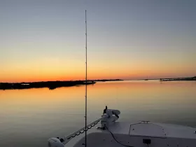 A serene sunset view from the bow of a fishing boat, showcasing calm waters and a picturesque horizon — perfect for evening cruises.