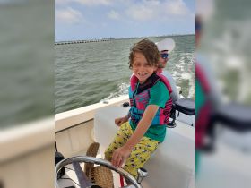 A young boy smiles while steering a boat, showcasing the joy of boating adventures. Perfect for family outings on the water.