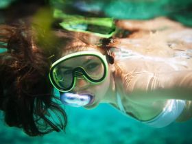 A young girl enjoys snorkeling underwater, showcasing the vibrant marine life and clear turquoise waters — a perfect moment for aquatic adventures.