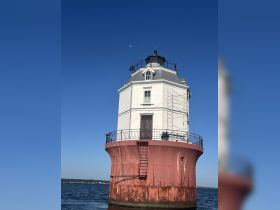 A lighthouse stands prominently against a clear blue sky, showcasing its unique architecture. The image captures the structure's details but lacks clarity.