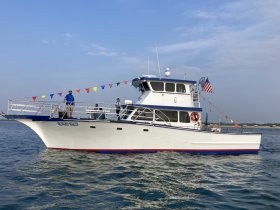 A spacious vessel named 'Crunch Time' is seen underway, showcasing its vibrant decorations and crew members enjoying the day on the water.