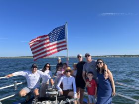 A joyful family poses together on a boat with an American flag waving in the background, capturing a memorable day on the water.
