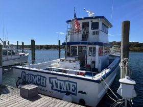 The 'Crunch Time' boat is docked at the marina, showcasing its vibrant design and structure against a clear blue sky — perfect for fishing trips or charter services.