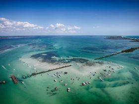 A stunning aerial view of a vibrant coastline dotted with boats, showcasing the beautiful turquoise waters and sandy shallows — perfect for exploring the scenic waterways.