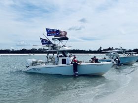 A lively group enjoys a beach day with multiple boats anchored in shallow water, perfect for socializing and fun in the sun.