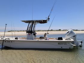 A side view of a Carolina Skiff boat docked in shallow waters, showcasing its sleek design and fishing equipment, perfect for a day of angling adventures.
