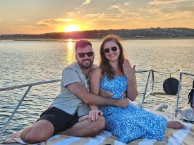 A couple celebrates their engagement on a boat at sunset, showcasing a romantic moment perfect for memorable cruises.