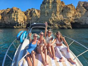 A joyful group of friends celebrates on the deck of a boat with cocktails, surrounded by stunning coastal cliffs — perfect for memorable outings and celebrations on the water.