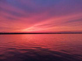 A breathtaking sunset paints the sky in vibrant hues over calm waters, creating a picturesque backdrop for evening boat trips.
