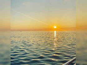 A serene sunset view over calm waters, with a distant boat visible on the horizon — perfect for tranquil evening cruises.