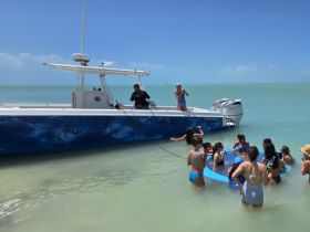 A lively group enjoys a fun day at the beach, interacting with a boat and engaging in water activities — perfect for memorable summer outings.