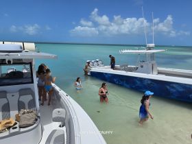 A lively group enjoys a beach day with two boats anchored nearby, showcasing fun in the sun and swimming in clear waters.