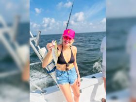 A woman proudly displays her catch while fishing on a boat, showcasing the excitement of a day out on the water.