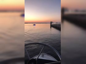 A serene sunset view from the helm of a boat, capturing the tranquil waters and a distant vessel, perfect for evening cruises.