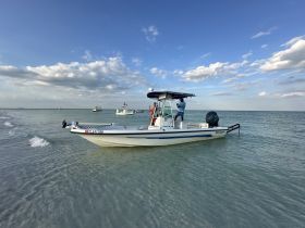 A boat is anchored in shallow waters with people onboard, enjoying a day out on the water — perfect for fishing or leisure activities.