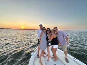 A joyful group of friends poses together on a boat at sunset, capturing the essence of a perfect evening celebration on the water.