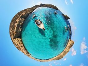 A stunning panoramic view of a group enjoying a boat trip in crystal-clear waters surrounded by rocky cliffs — perfect for island adventures and swimming excursions.