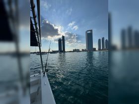 A scenic view from the side of a boat, showcasing the skyline of a city with modern skyscrapers and a fishing rod in the foreground — perfect for a day out on the water.