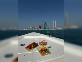 A beautifully arranged selection of fruits and snacks on the deck of a boat, with a stunning city skyline in the background — perfect for a luxurious day on the water.