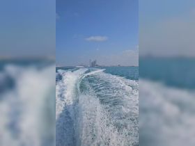 A stunning view of a boat underway, leaving a wake in the clear blue waters with a city skyline in the background, perfect for showcasing scenic boat rides.